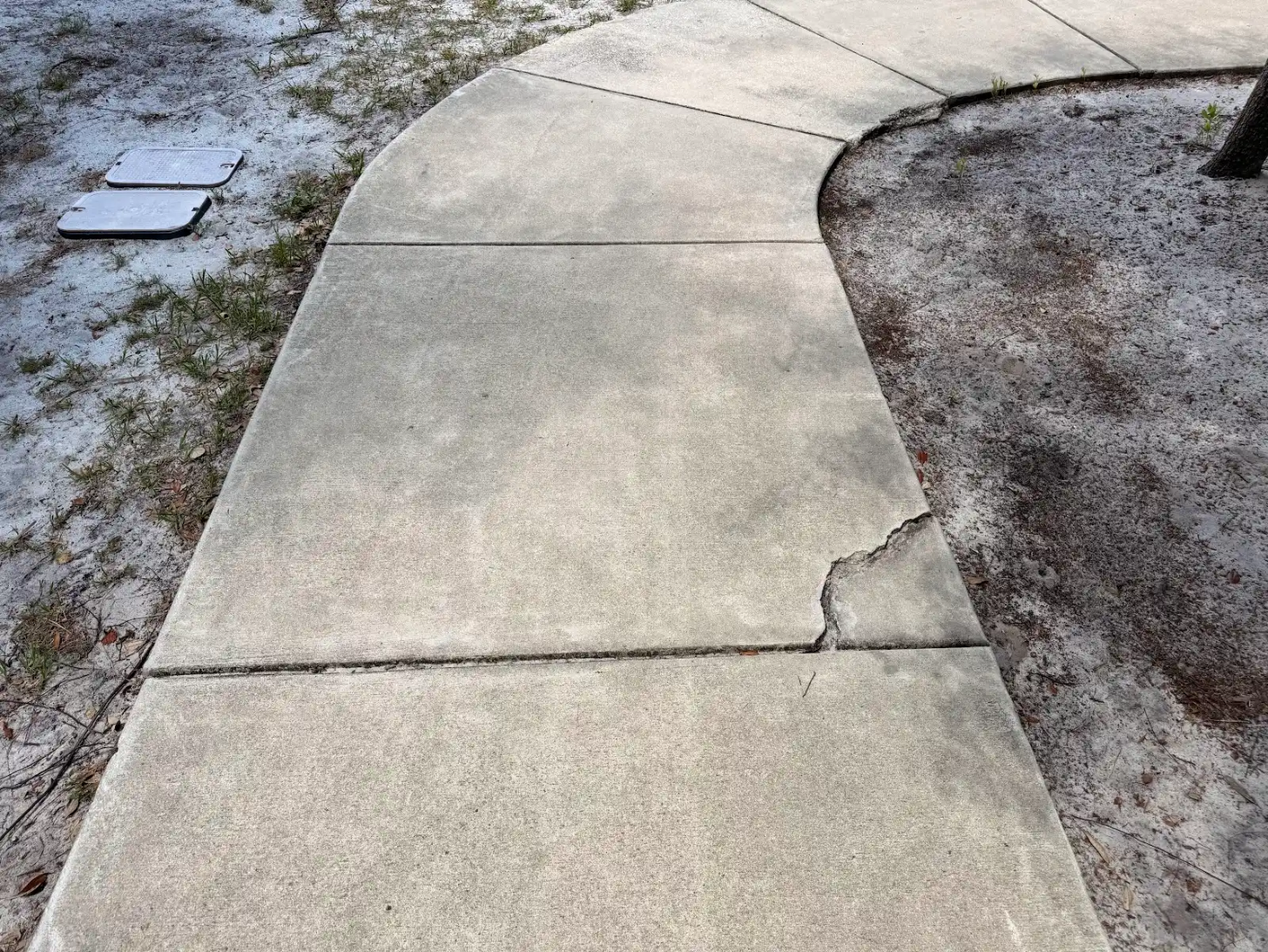 A curving concrete sidewalk with a chipped, crumbling corner, the kind of surface damage a patch alone will not hold